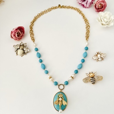 Colar com contas turquesa e corrente dourada com pendente de abelha e três broches de insetos dourados com pérolas e strass.