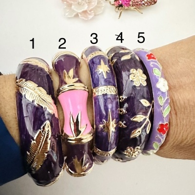 Cinco pulseiras coloridas com detalhes dourados, numeradas de 1 a 5, usadas num braço.