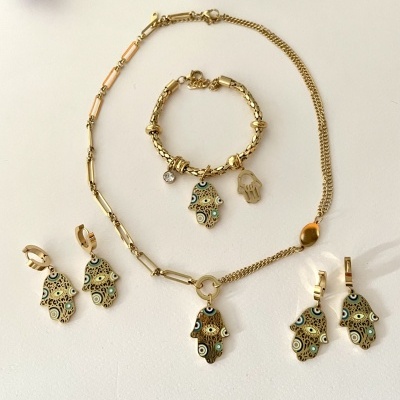 Conjunto joias douradas com padrão verde e preto em superfície branca com flores ao fundo