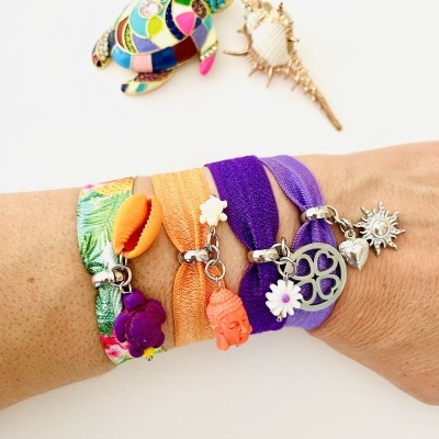 Braço com pulseiras elásticas coloridas com pendentes e tartaruga colorida ao fundo.