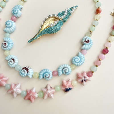 Colares com contas coloridas e broche de concha cravejado em fundo bege