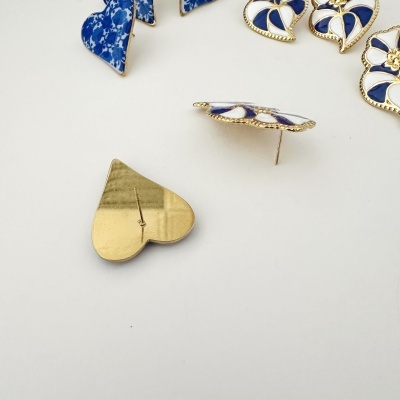 Brincos de pinos com formas de coração e flores em azul, branco e dourado sobre fundo branco