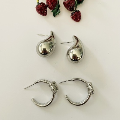 Broche de morangos dourado e dois pares de brincos prateados sobre fundo branco