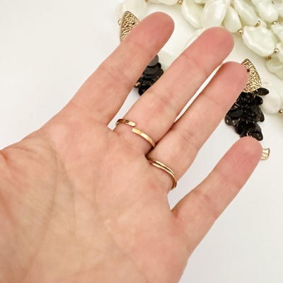 Anel dourado aberto numa mão com brincos pretos e dourados ao fundo