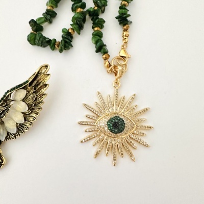 Colar com pendente dourado em forma de olho e contas verdes, em fundo branco.