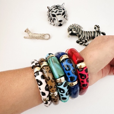 Pulseiras grossas com padrão animal print e três broches de metal em fundo branco
