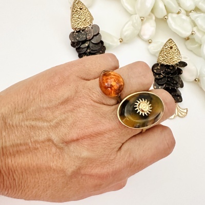 Mão com dois anéis e dois brincos dourados e pretos sobre fundo branco