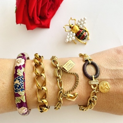 Conjunto de pulseiras coloridas e douradas com uma rosa vermelha e broche de abelha no fundo branco