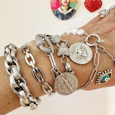 Vários braceletes prateados no braço com medalha e pingentes distintos