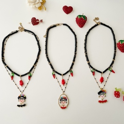 Três colares pretos com pingentes femininos pixelados e objetos decorativos vermelhos