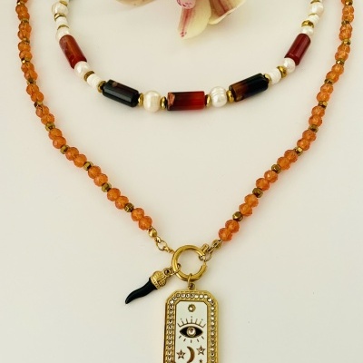 Dois colares com diferentes contas e um pingente dourado com símbolo de olho sobre fundo branco