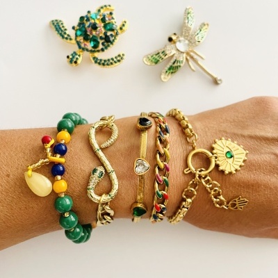 Pulseiras coloridas e douradas no pulso com duas broches douradas ao fundo