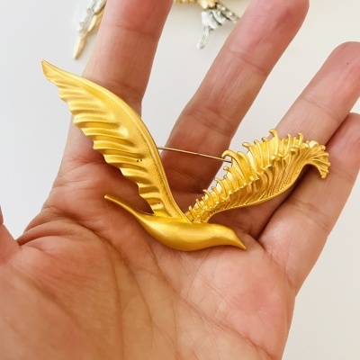 Broche dourado em forma de pássaro com asas estendidas sobre uma mão