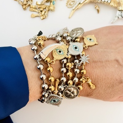 Pulseiras metálicas douradas e prateadas com motivos de olhos e estrelas no pulso