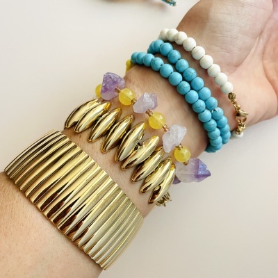 Pulseiras coloridas e bracelete dourado no pulso de uma pessoa