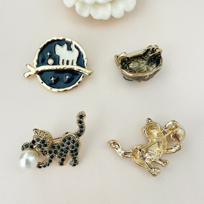 Conjunto de quatro pins dourados com gatos e um círculo azul, em superfície branca com flor branca.
