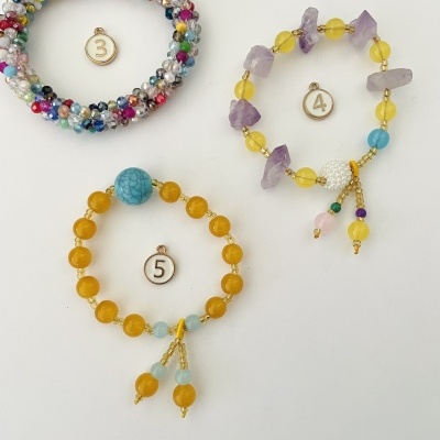 Três pulseiras coloridas feitas com pedras e contas, com etiquetas numeradas ao lado