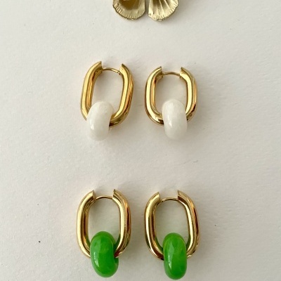 Dois pares de brincos dourados com pendentes branco e verde, com flor decorativa ao fundo