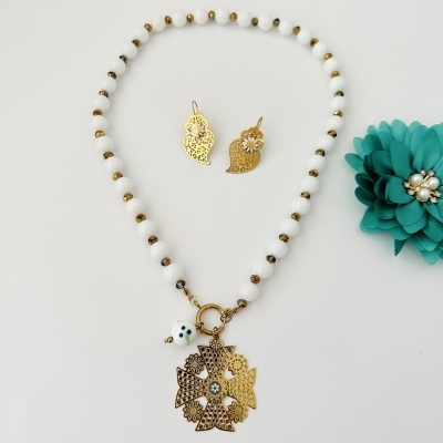 Conjunto de colar e brincos dourados com contas brancas e douradas e flor verde com pérolas.