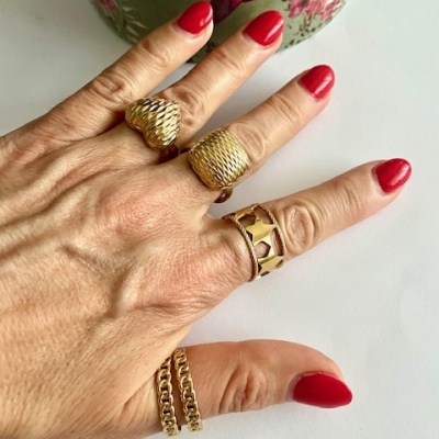 Mão com anéis dourados e unhas vermelhas em fundo branco com caixa decorativa verde.