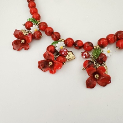 Colar artístico com contas vermelhas e flores decorativas em fundo branco