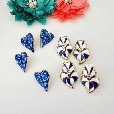 Brincos em azul, branco e dourado com padrão floral e formato coração