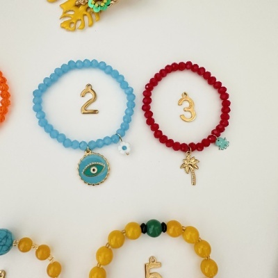 Pulseiras azul e vermelha com pendentes dourados sobre fundo branco