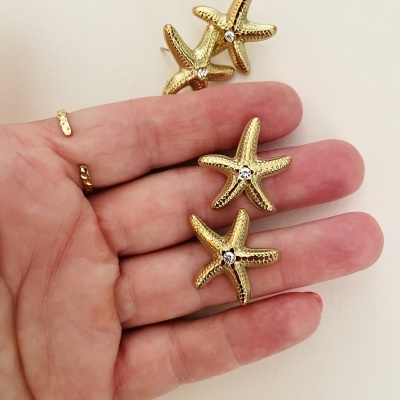 Brincos dourados em forma de estrelas do mar com pedras brilhantes no centro
