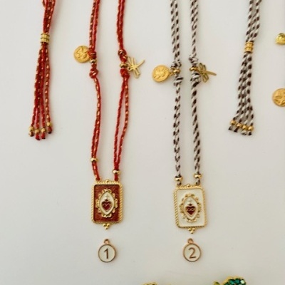 Colares com cordões vermelhos e pretos e pendentes dourados, broche de borboleta colorido.