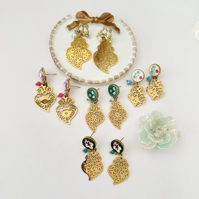 Seis pares de brincos dourados com padrões recortados e detalhes florais coloridos sobre fundo branco