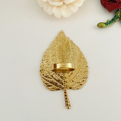 Suporte de vela em metal dourado em formato de folha sobre superfície branca com flores decorativas próximas