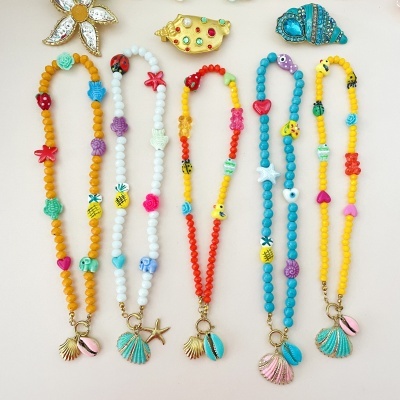 Cinco pulseiras coloridas com conchas e búzios, sobre fundo branco.