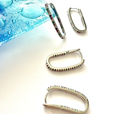 Brincos prateados com pedras coloridas e objeto azul com gotas