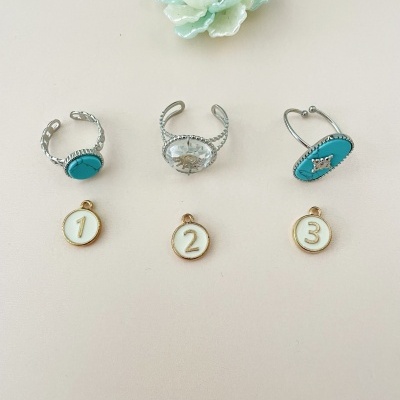 Anéis e medalhas numeradas dispostos sobre fundo bege com flor decorativa branca