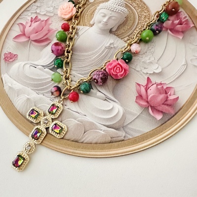 Colar com cruz dourada e contas coloridas sobre prato decorativo com Buda e flores de lótus