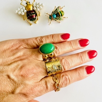 Anel dourado com pedra verde e broches de abelhas em fundo branco