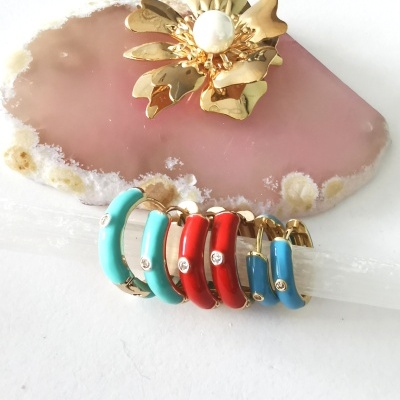 Brincos coloridos em metal dourado com esmalte e cristais sobre pedra rosa