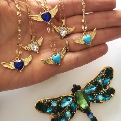 Colares dourados com pingentes de asas e corações coloridos e broche de libélula com pedras coloridas