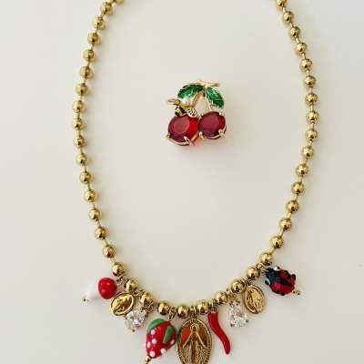Colar dourado com pendentes coloridos e broche de cerejas vermelhas com folhas verdes