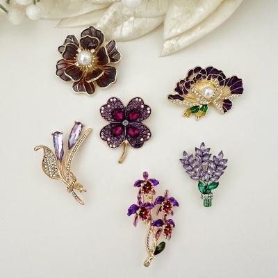 Broches florais decorativos com pedras roxas e pérolas sobre fundo branco.