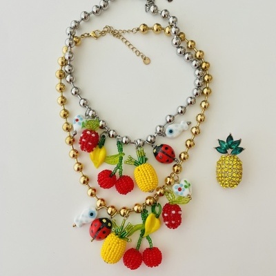 Colares metálicos com pendentes de frutas coloridas e um brinco de abacaxi amarelo