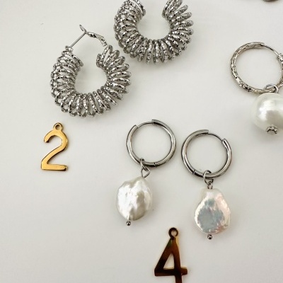 Brincos prateados com textura ondulada e pérolas em fundo branco com pendentes dourados número 2 e 4