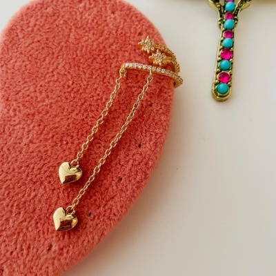 Anel de ouro com dois corações pendurados sobre tecido rosa e crucifixo decorativo colorido