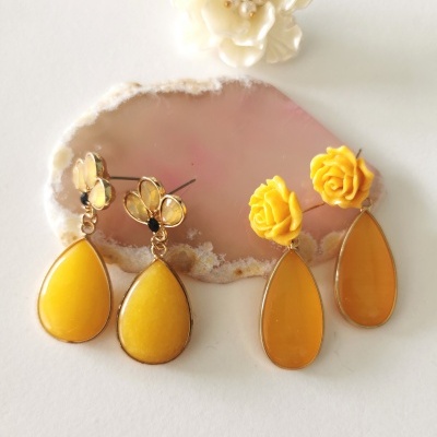 Dois pares de brincos amarelos com flores e gotas amarelas sobre pedra de geodo rosa