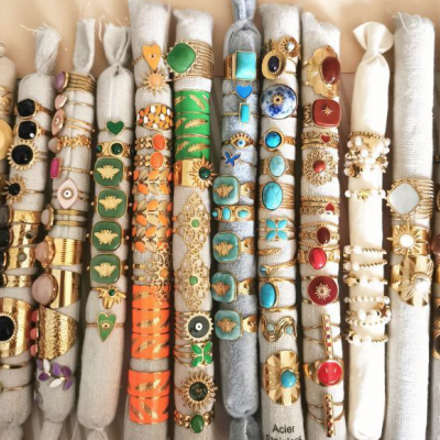 Pulseiras e anéis coloridos em rolos de tecido creme com padrões dourados e texturas variadas