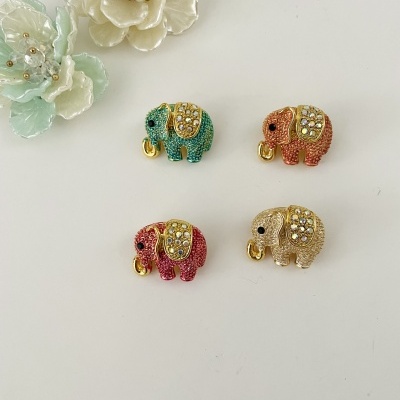 Quatro pendentes coloridos em forma de elefantes com cristais sobre superfície branca e flores decorativas