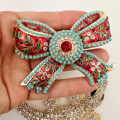 Broche laço colorido com pedras e esmalte, segurado numa mão
