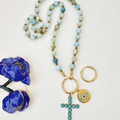 Colar azul esverdeado com cruz e medalhão dourado, junto a flor azuis em esmalte