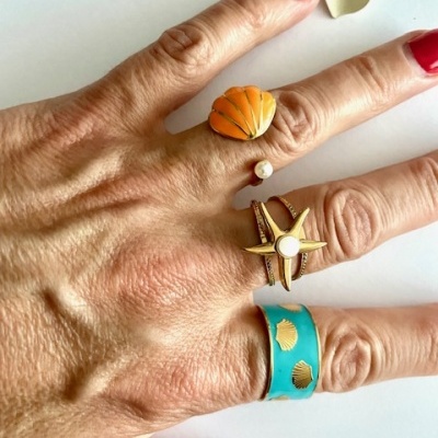 Mão com três anéis coloridos de inspiração marítima e flor amarela