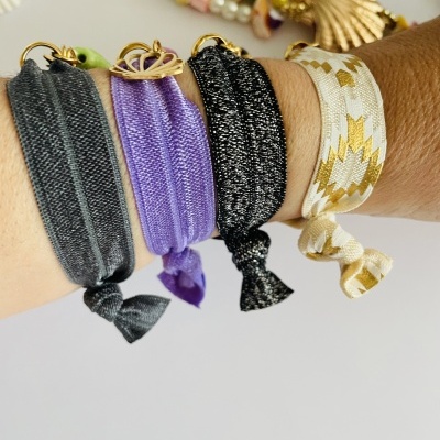 Pulseiras elásticas coloridas e brilhantes no pulso com fundo branco e colares coloridos desfocados